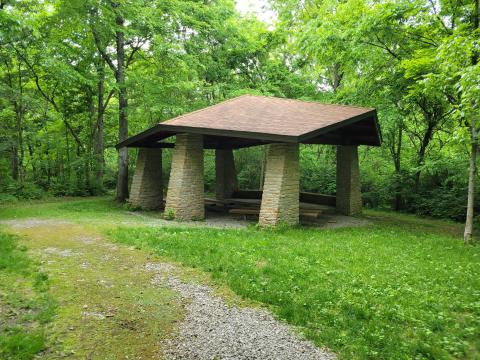 An image of the Boone County Nature Center Shelter surrounded by lush forest and green grass. 